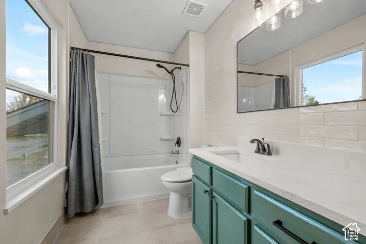 White subway tile surround, integrated bathtub and shower, light-toned floor tile, white countertop, and teal vanity with dark hardware