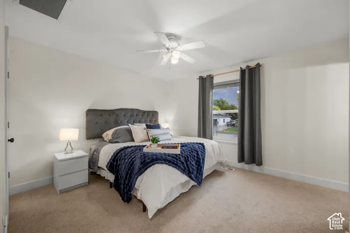 Plush carpet flooring, ceiling fan with integrated lighting, window with dark-toned drapes, and white baseboard trim