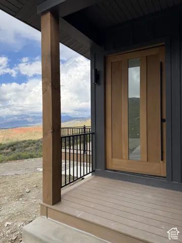 Wood-paneled entry door with vertical glass insert, dark exterior siding, black railing, durable deck flooring, and a substantial wood support column
