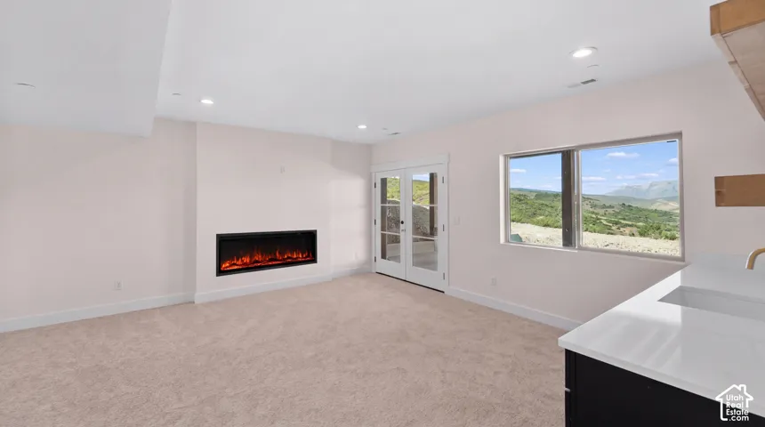 Electric fireplace, recessed lighting, carpeted flooring, double French doors, and a built-in wet bar with a single basin sink