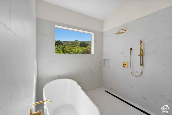 Freestanding soaking tub with gold-finish fixtures, a walk-in shower with gold-finish rain shower head, and floor-to-ceiling veined white tiling