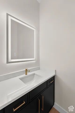 Backlit mirror, integrated sink, gold-finish faucet, black cabinetry, and gold-finish hardware