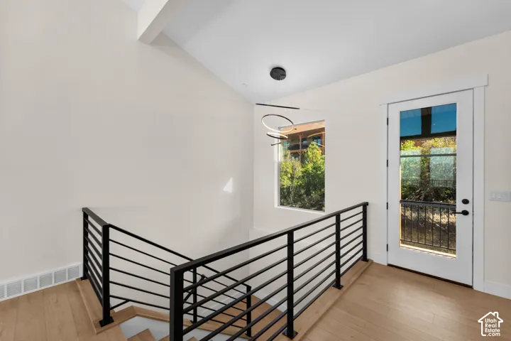 Modern open-tread staircase with black metal railings, light wood-finish flooring, and a contemporary ceiling fixture