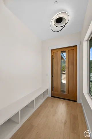 Entryway featuring wood-finish flooring, a contemporary ceiling light fixture, a built-in storage bench, and a solid wood entry door with a window insert