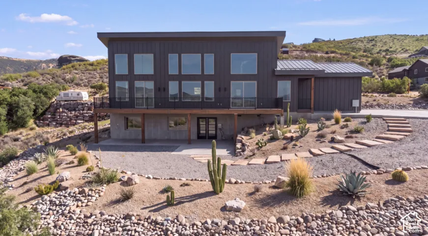 Modern exterior with extensive fenestration, elevated balcony with black railings, and a gravel driveway