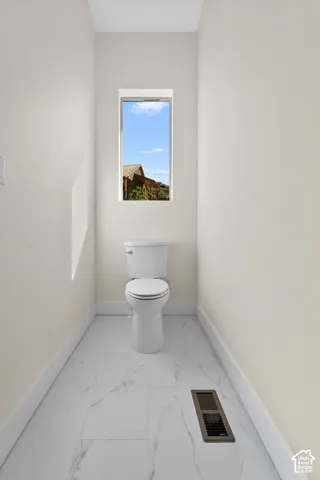 Rectangular window, neutral wall paint, white toilet, white baseboards, and patterned floor tile