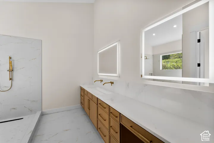 Dual vanity with illuminated mirrors, expansive white countertop, wood-finish cabinetry, and gold-finish fixtures
