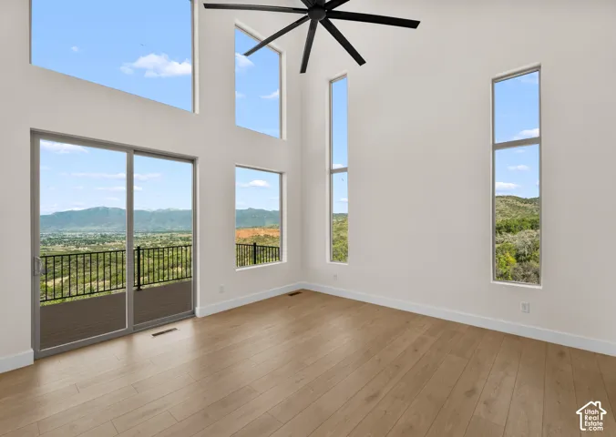 Vaulted ceilings featuring a ceiling fan, a sliding glass door opening to a deck with a metal railing, wood-finish flooring, and multiple tall windows