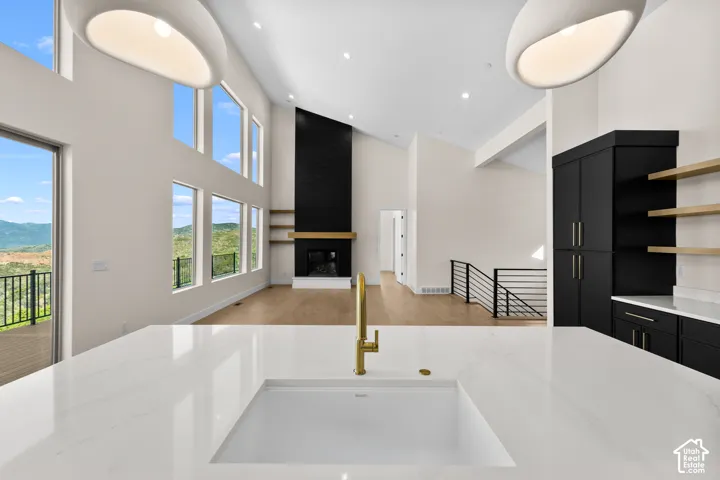 High ceilings with abundant natural light, a contemporary fireplace with a wood mantle, wood-finish flooring, and a kitchen island with an integrated sink and gold-tone faucet