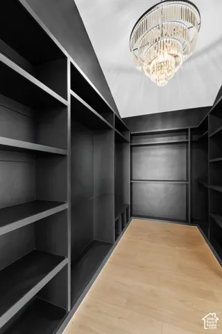Walk-in closet featuring extensive built-in shelving, hanging rods, light wood-finish flooring, and a tiered chandelier