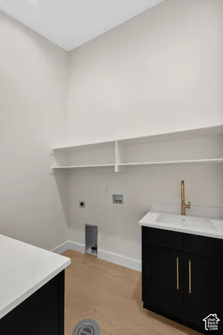 Laundry room featuring built-in shelving, wood-finish flooring, a utility sink with a gold-tone faucet, and dark cabinetry with a light-toned countertop
