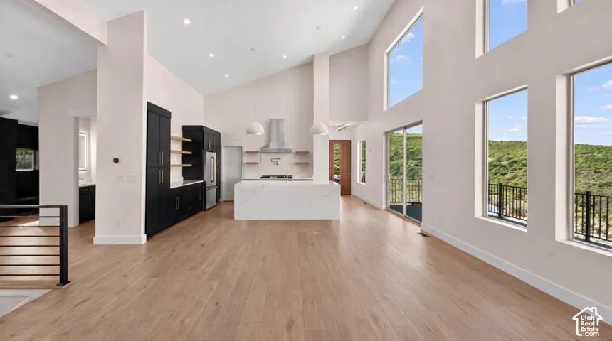 Vaulted ceilings, wood-finish flooring, a contemporary kitchen with a center island, extensive windows, and a sliding glass door to a balcony
