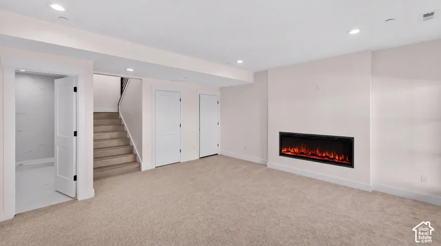 Recessed electric fireplace, light-colored carpeting, multiple paneled doors, staircase with dark railing, and recessed lighting