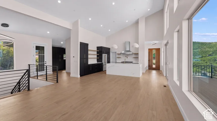Open-concept living space featuring vaulted ceilings, wood-finish flooring, a contemporary kitchen with a waterfall island, and large picture windows
