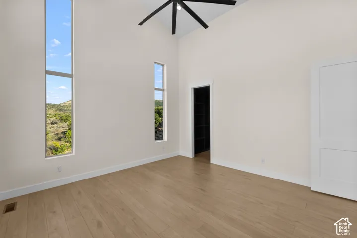 Vaulted ceiling with exposed beam, wood-finish flooring, full-height vertical windows, and a ceiling fan