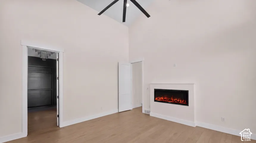 Vaulted ceiling with a ceiling fan, wood-finish flooring, built-in electric fireplace, and a walk-in closet with built-in shelving