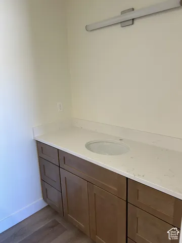 Bathroom vanity with a white undermount sink, light-toned countertop, wood-finish cabinetry, and overhead lighting fixture