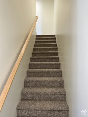 Carpeted staircase featuring a light wood handrail and neutral wall tones