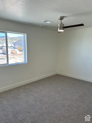 Neutral-toned carpeting, a modern ceiling fan with integrated lighting, and a large window providing natural light
