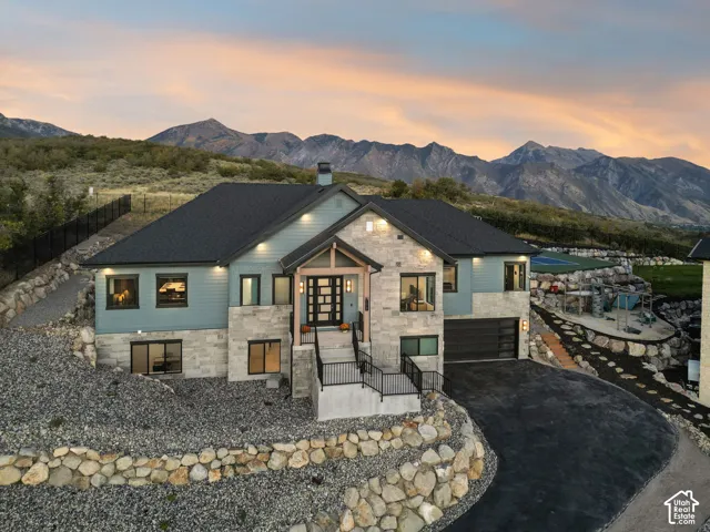 Stone and siding exterior with a multi-level design, attached garage, paved driveway, and established rock landscaping