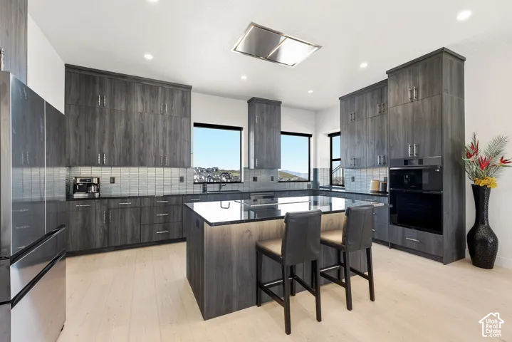 Kitchen featuring wood-finish cabinetry, light wood-finish flooring, built-in stainless steel appliances, and a central island with a dark countertop