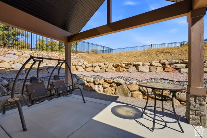 Covered patio with concrete flooring, supported by a stone-clad column, overlooking a rock retaining wall and gravel landscaping