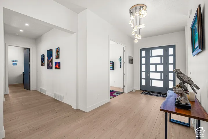 Contemporary entry with light wood-finish flooring, a modern glass-paneled front door, and a multi-bulb chandelier