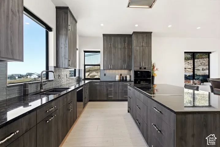 Kitchen featuring extensive wood-finish cabinetry, black granite countertops, a large center island, built-in appliances, and light wood-finish flooring