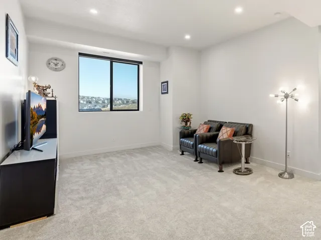 Recessed lighting, large window with a dark frame, light-colored carpeting, white wall finishes, and a doorway to an additional room