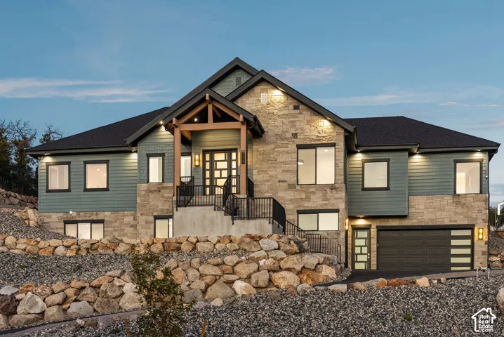 Exterior featuring stone and siding finishes, an inviting front entry with a covered porch, an attached garage, and multiple windows