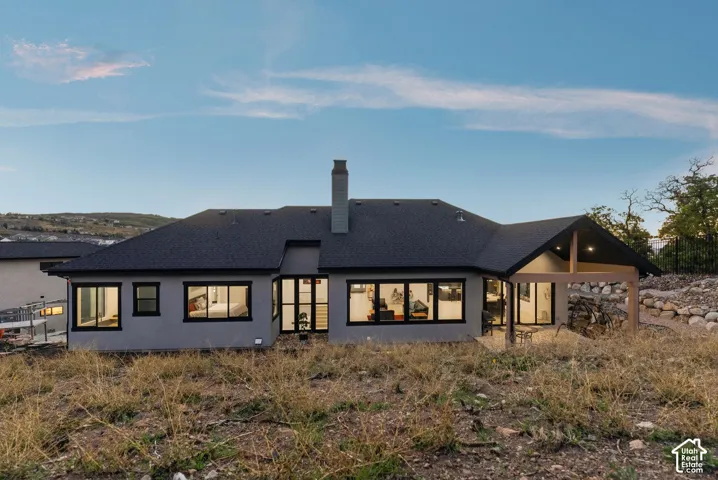 Expansive rear exterior featuring a covered patio, multiple large windows, and a dark shingle roof