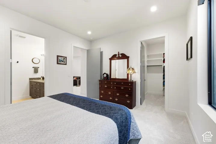Recessed lighting, light-toned carpeting, built-in shelving, wood-finish vanity with stone countertop, and a large window