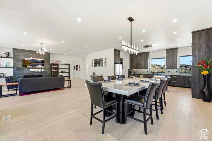 Open concept living area featuring light wood-finish flooring, recessed lighting, a stone-finish accent wall with integrated fireplace, a modern linear chandelier, and dark wood-grain cabinetry