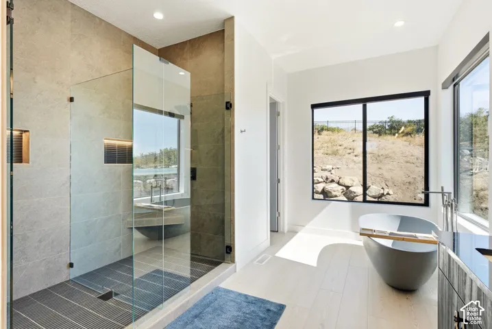 Spacious bathroom featuring a glass-enclosed shower with tiled walls and floor, a freestanding soaking tub, and large windows