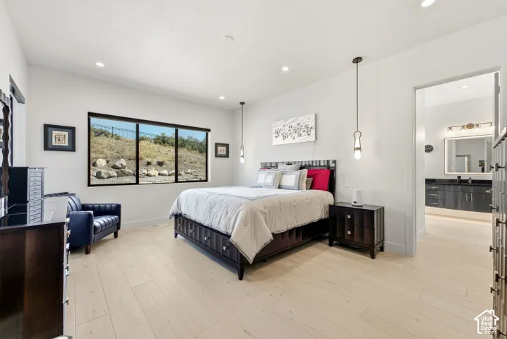 Light wood-finish flooring, recessed lighting, expansive window with natural scenery, pendant lighting, and an entryway to an attached bathroom