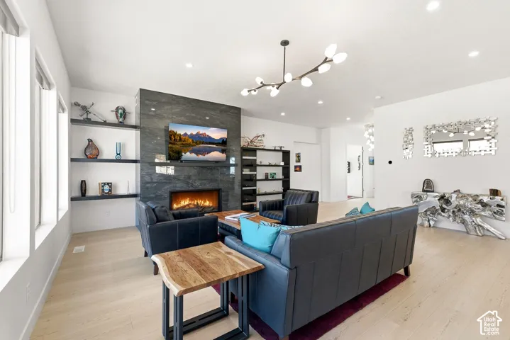 Spacious living area featuring light wood-finish flooring, a contemporary fireplace with a dark stone-clad surround, and multiple recessed ceiling lights