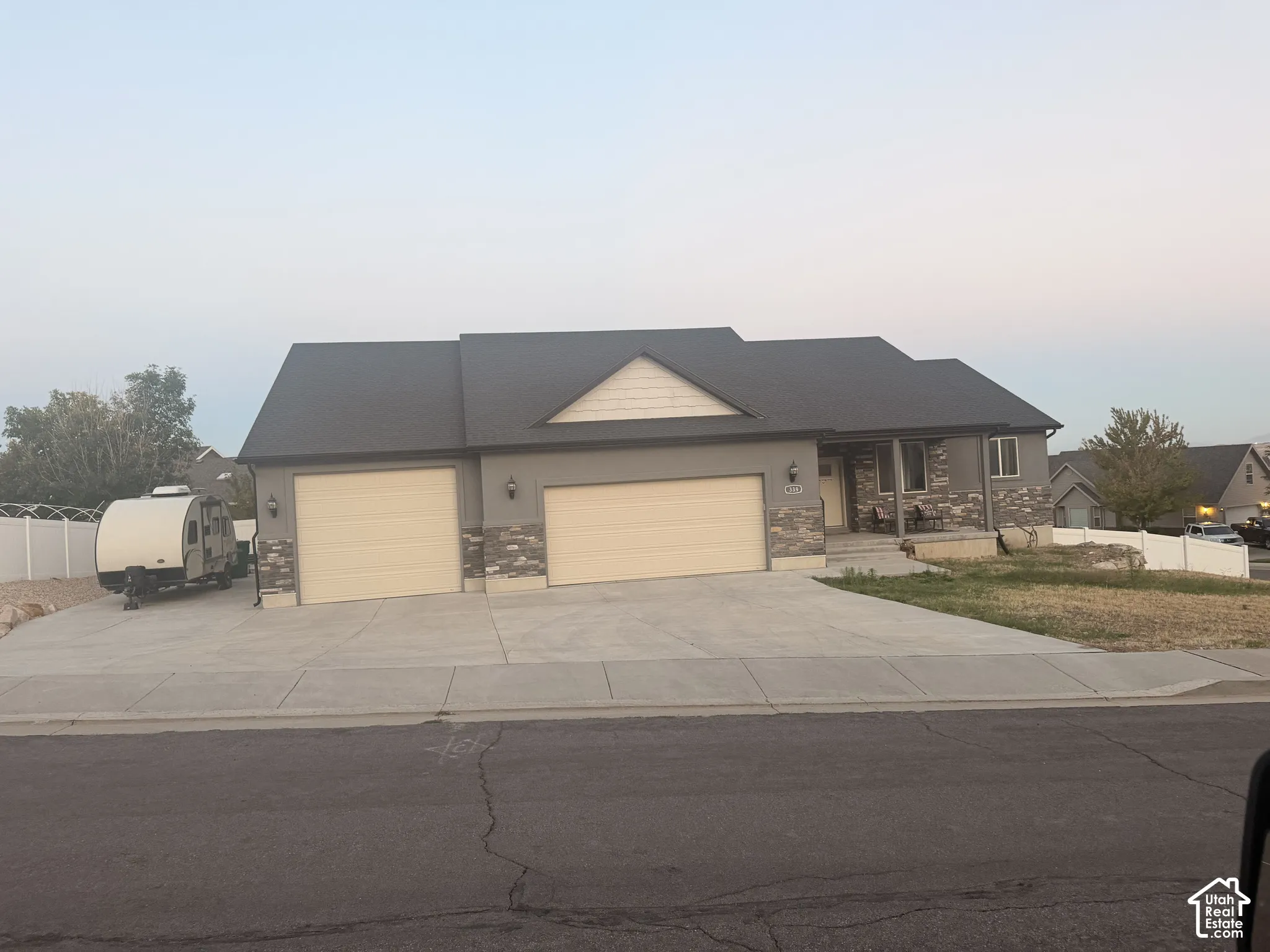 Two-car garage, concrete driveway, stone facade accents, covered entry, and dark shingle roof
