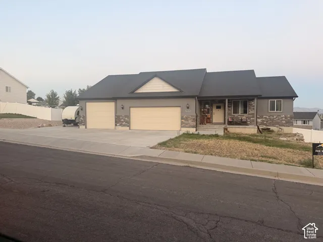 Contemporary ranch-style residence featuring a dual garage, a covered front porch, and a stone facade accent