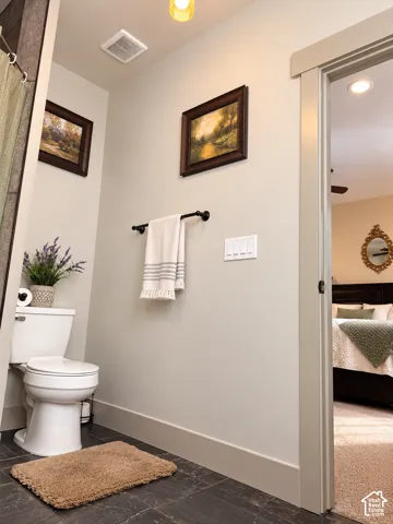 White toilet with a dark tile floor, recessed lighting, and a towel bar
