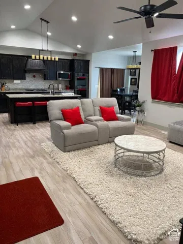 Vaulted ceilings, recessed lighting, wood-finish flooring, dark cabinetry, and a kitchen island with seating