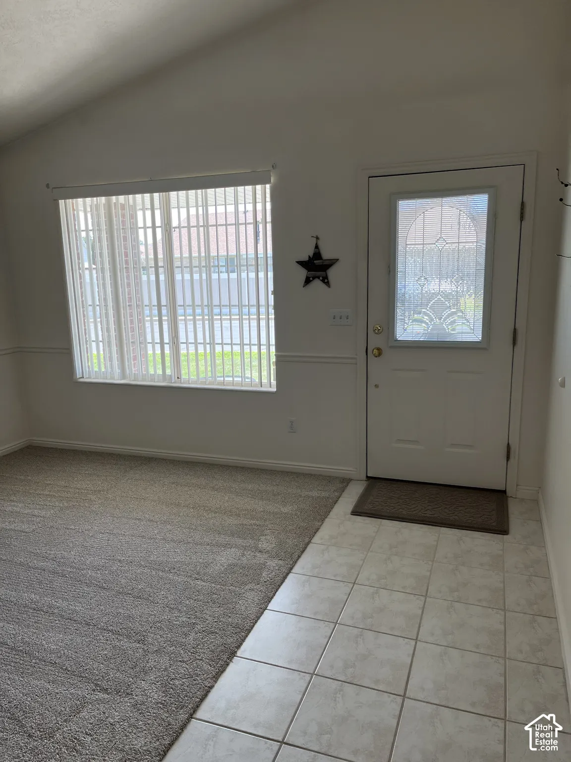 Vaulted ceiling, paneled entry door with decorative glass insert, tiled entryway, window with vertical blinds, and wall paneling