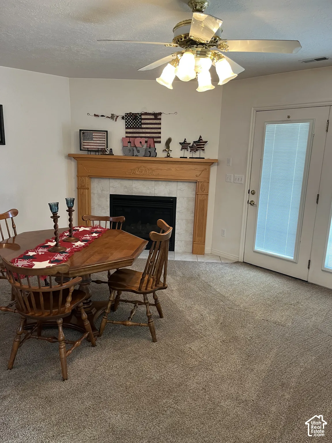 Recessed fireplace with tile surround, wood mantel, ceiling fan with lighting, and carpet flooring