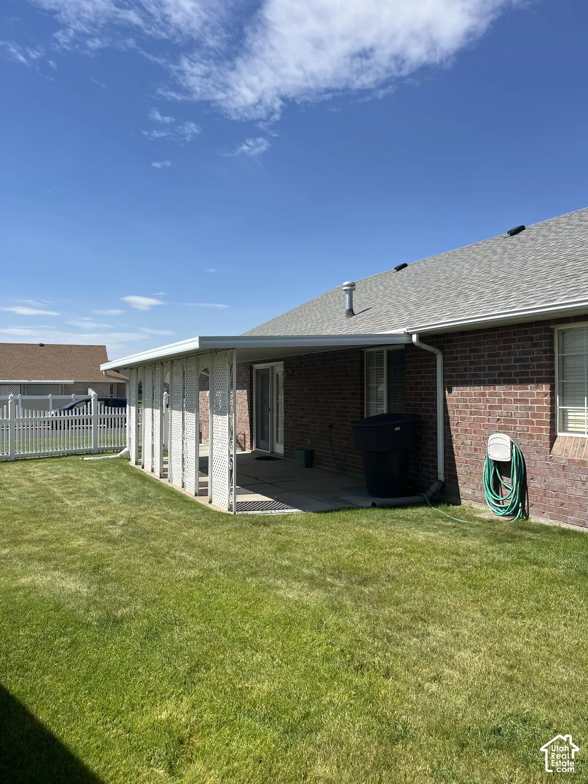 Expansive grassy yard with a covered patio, brick exterior, and white picket fencing