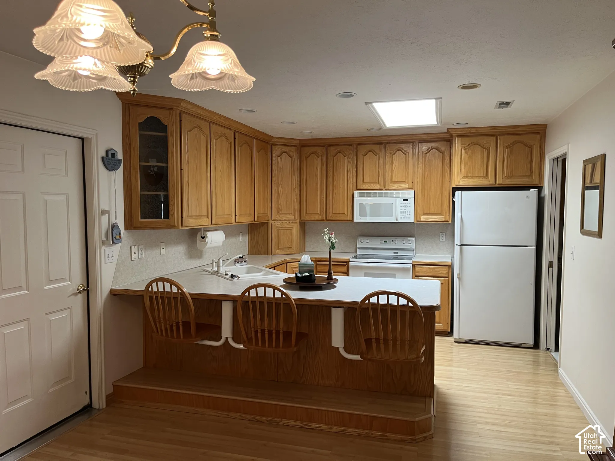 Kitchen featuring wood-finish cabinetry, white countertops, built-in appliances, a breakfast bar with stepped wood-finish flooring, and a ceiling-mounted light fixture