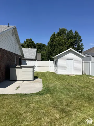 Expansive lawn area with a white privacy fence, concrete patio, and a dedicated storage shed