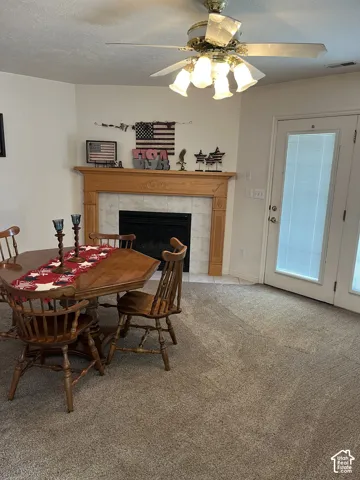 Recessed fireplace with tile surround, wood mantel, ceiling fan with lighting, and carpet flooring