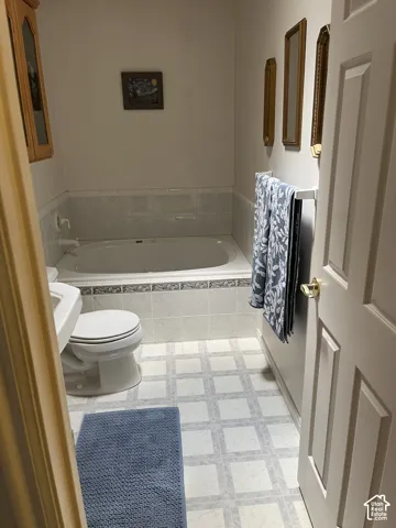 Built-in bathtub with tiled surround, patterned floor covering, and a paneled door