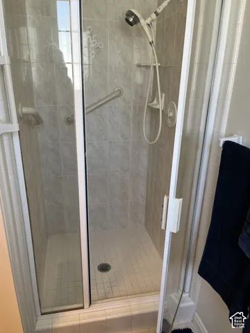 Tiled shower enclosure with a glass door, grab bars, and a handheld showerhead