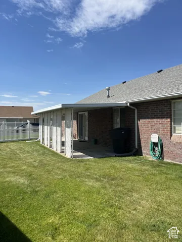 Expansive grassy yard with a covered patio, brick exterior, and white picket fencing