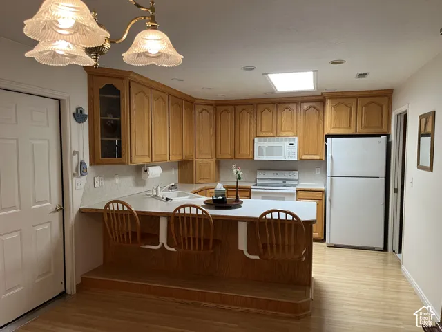 Kitchen featuring wood-finish cabinetry, white countertops, built-in appliances, a breakfast bar with stepped wood-finish flooring, and a ceiling-mounted light fixture